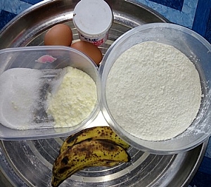 A tray containing sifted flour, milk, sugar, eggs, baking powder and ripe bananas