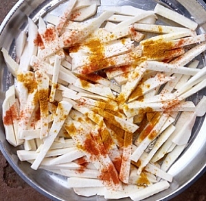 Yam chips in a tray being sprinkled with salt, chilli pepper and curry powder
