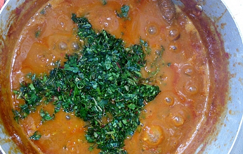 Shredded yakwa and spinach being added to miyan taushe (pumpkin soup)