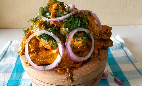 Serve Isi Ewu in a wooden bowl and garnish with onion rings and Utazi