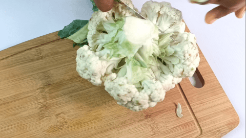 Use a knife to cut off the greenish leaves of the cauliflower leaving only the white head